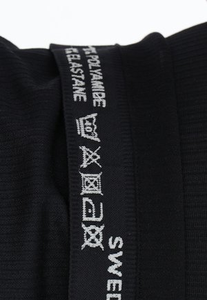 Sort tekstil med ribbet struktur, der har hvide broderede labels med plejemærker og teksten "SVERIGE". Stofsammensætningen inkluderer polyamid og elastan.