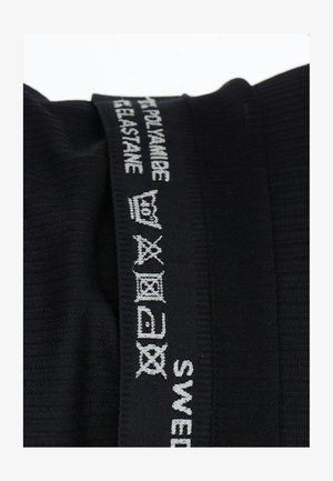 Tessuto nero con texture a coste, caratterizzato da etichette ricamate bianche con simboli di cura e testo "SWEDEN". La composizione del tessuto include poliammide ed elastan.