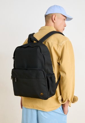 Czarny plecak wykonany z trwałego materiału, z kieszenią na zamek z przodu, regulowanymi szelkami i małym akcentem logo w dolnej części.