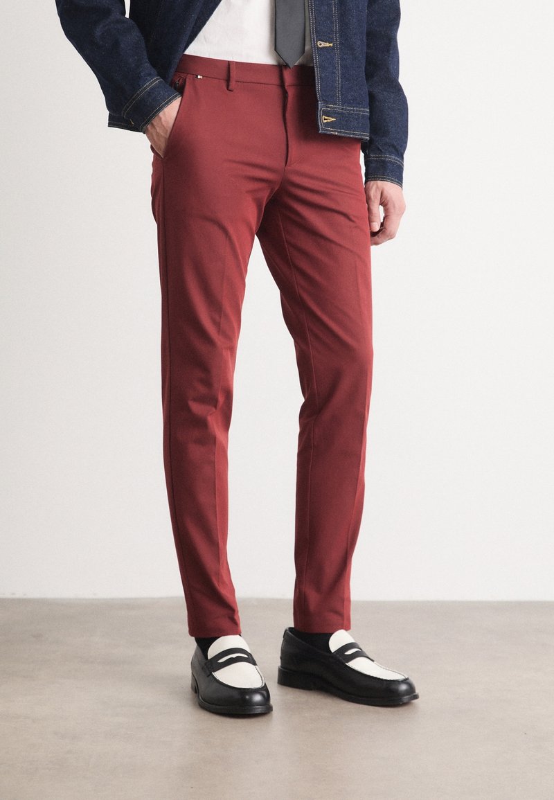 Czerwone wąskie spodnie wykonane z lekkiego materiału, z płaskim przodem, bocznymi kieszeniami i wyraźnymi detalami przeszyć. Zestawione z czarno-białymi mokasynami.