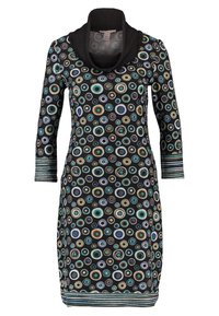 Czarna sukienka z kolorowymi koncentrycznymi okręgami w odcieniach niebieskiego, zielonego i brązowego. Posiada wycięcie w kształcie cowl oraz rękawy o długości 3/4 z paskowanymi mankietami.