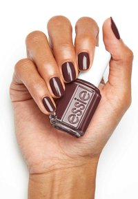 Vernis à ongles Essie dans une teinte bordeaux foncé, finition brillante, tenu dans une main avec des ongles manucurés peints dans la même couleur.