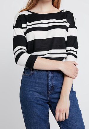Haut rayé noir et blanc avec un col bateau et des manches trois-quarts, associé à un jean bleu taille haute. Texture de tissu lisse.