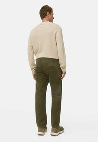 Beige overhemd met lange mouwen en donkergroene corduroybroek, met een relaxte pasvorm en achterzakken, gecombineerd met tan sneakers.