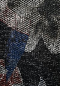 Stricktextil mit einer Mischung aus Schwarz, Grau, Blau und Rot sowie abstrakten Mustern; strukturierte Oberfläche mit sichtbaren Nähdetails.