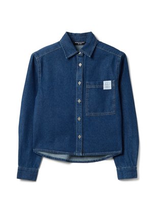 Chemise en denim bleu foncé à boutons, manches longues, une poche poitrine frontale, et une petite étiquette blanche sur le coin supérieur droit de la poche.