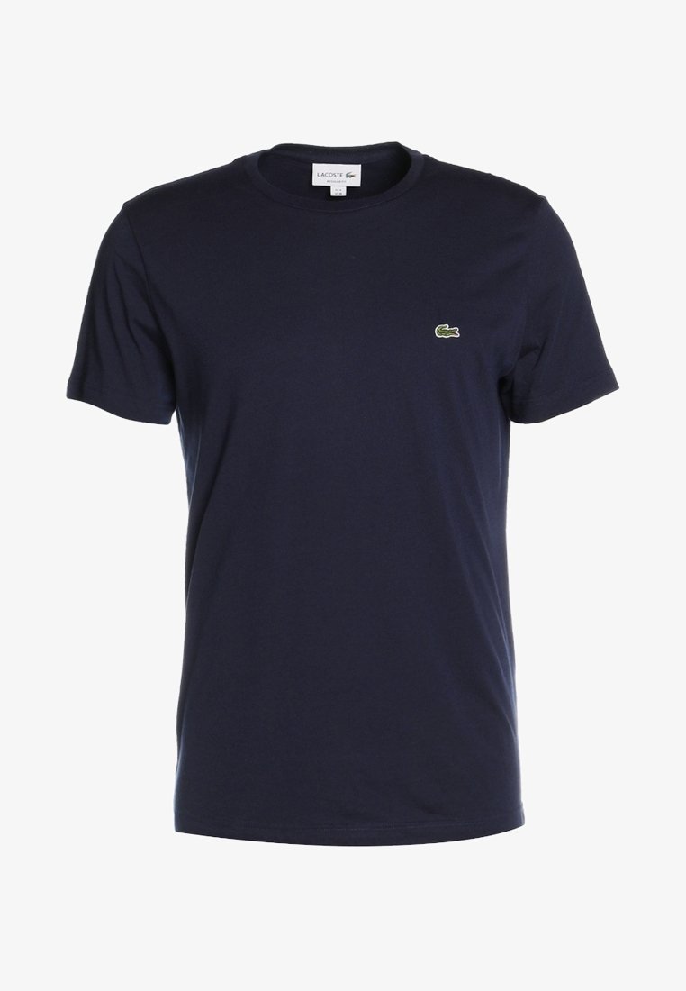 T-shirt bleu foncé à manches courtes col rond avec un petit logo crocodile vert sur la poitrine gauche et une étiquette de marque blanche à l'intérieur du col.