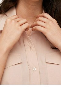 Chemise button-up rose clair à manches courtes, dotée de deux poches poitrine et d'un tissu lisse, légèrement texturé.