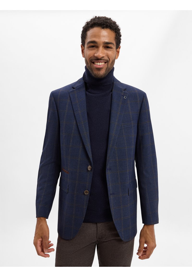 Marineblau kariertes Blazer mit zwei Knöpfen, braunen Akzenten und einer taillierten Passform. Getragen über einem dunklen Rollkragenpullover und braunen Hosen.