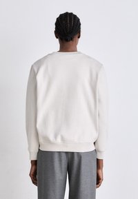 Lys grå sweatshirt med ribbede mansjetter og kant, laget av mykt materiale. Enkel design med rund hals og ingen synlige grafikker.