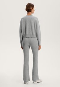 Grauer Strickpullover mit einem verkürzten Design und geripptem Saum, kombiniert mit passenden grauen Schlaghosen aus demselben Material.