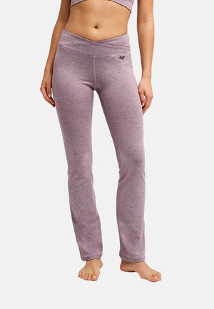 Femme portant un pantalon de yoga taille haute mauve chiné avec une ceinture croisée, debout pieds nus sur un fond uni.