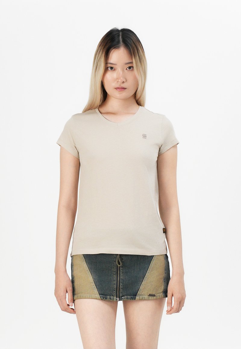Beige short-sleeved t-shirt with a round neckline and small logo on the chest, paired with a denim skirt featuring color-blocking design.