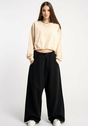 Jasnobeżowy, krótki sweatshirt z długimi rękawami i elastycznym dołem, w połączeniu z luźnymi czarnymi spodniami i białymi sneakersami.