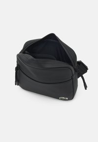 Borsa a tracolla nera in tela con superficie testurizzata, chiusura a doppia zip, scomparti interni e una piccola etichetta logo sul davanti.