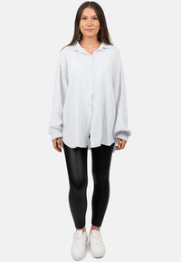 Oversized witte blouse met een structuurstof, lange mouwen en een kraag, gecombineerd met zwarte legging en witte sneakers.