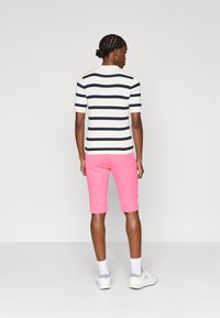 Top de malha às riscas em branco e azul marinho, combinado com calções cor-de-rosa. A modelo está de costas para a câmara, usando ténis brancos.