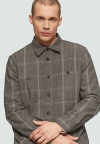 Grijze geruite flanellen shirt met een knoopsluiting aan de voorkant, kraag, zak en contrasterende witte strepen. Zachte textuur en een relaxte pasvorm.