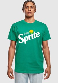 Grøn bomulds T-shirt med kortærmer, der har et stort hvidt "Sprite" logo og en gul limegrafik over teksten.