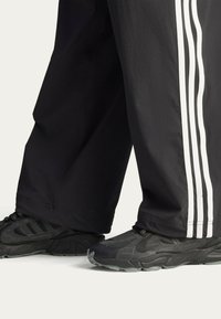 Black athletic shoes with textured detailing and black pants featuring white side stripes. Shoes have a rugged sole and laces.