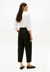 Witte blouse met lange mouwen, zwarte high-waisted broek en zwarte flats. De stof lijkt glad; de broek is op maat gemaakt met een cropped zoom.
