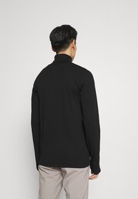 Zwarte lange mouwen shirt met een hoge kraag, gladde textuur en een getailleerd ontwerp, gezien vanaf de achterkant tegen een effen achtergrond.