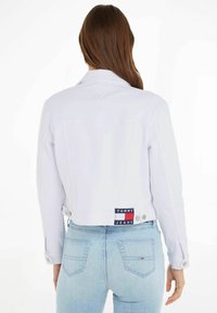 Vit denimjacka med knappstängningar, croppad design och tvåfärgad märkespatch på baksidan. Slät textur och figurnära passform.