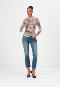 Long-sleeve top featuring a colorful print of vintage labels. Paired with mid-rise, faded blue jeans and black pointed heels.