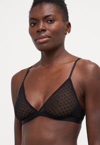 Svart trekant-bh laget av gjennomsiktig prikket mesh med blondekantdetaljer og justerbare stropper. Glatt underbånd for komfort.
