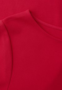 Gros plan sur un vêtement rouge montrant la texture du tissu, la couture de l'épaule et la finition de l'encolure ronde.