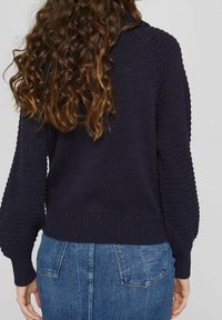 Pull en maille bleu marine avec des manches texturées et un ourlet côtelé, associé à une jupe en denim bleu avec des poches arrière.