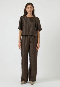 Conjunto marrón a juego que presenta un diseño texturizado y ondulado. La parte superior tiene mangas cortas y abullonadas y un corte corto, combinado con pantalones sueltos.