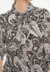 Black and beige blouse with paisley pattern, featuring a bow tie neck, long sleeves, and a lightweight fabric texture.