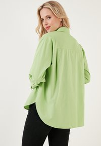 Camicia oversize verde chiaro con colletto, maniche lunghe e orlo arrotondato. Realizzata in un tessuto morbido con una texture liscia.