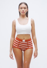 Λευκό crop top με ριμπ ύφανση, συνδυασμένο με πορτοκαλί και λευκά ριγέ σορτς υψηλής μέσης, που διαθέτουν ετικέτα με λογότυπο και έντονες ραφές.