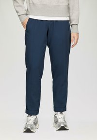 Marineblauwe broek met een taps toelopend ontwerp, gemaakt van een soepele stof, met voorplooien en omgeslagen benen. Gecombineerd met zilverkleurige sport schoenen.