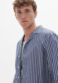 Kék és fehér csíkos ing, gallérral, gombos záródással, könnyű anyagból, enyhén strukturált és laza szabású.
