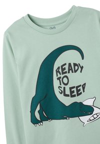 Lichtgroen longsleeve shirt met een dinosaurustekening en de tekst "KLAAR OM TE SLAPEN" in vetgedrukte zwarte letters. Zacht katoenmateriaal.