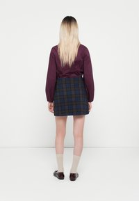 Bordeauxblouse met een riem en pofmouwen, gecombineerd met een blauwe geruite minirok, beige sokken en donkere schoenen. Eenvoudig ontwerp, gladde textuur.