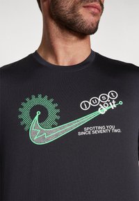 Černá dlouhá košile s grafickým designem, který obsahuje zelené akcenty, slogan "just do it" a stylizované prvky ozubeného kola a švihu.