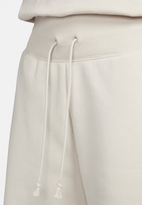 Los pantalones de chándal color beige claro presentan una cinturilla acanalada con un detalle de cordón y un tejido suave y texturizado para mayor comodidad.