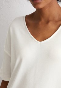V-neck, loose-fit t-shirt in soft, lightweight, off-white fabric. Features short sleeves and a smooth texture with subtle stitching details.