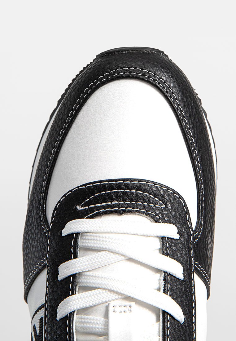 Gros plan d'un tennis noir et blanc avec des lacets blancs et des coutures noires contrastées sur des panneaux en cuir texturé.