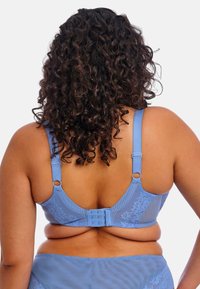 Sininen rintaliivi, jossa on monimutkaista kukkakuvioista pitsiä, säädettävät olkaimet ja takana koukku- ja silmukkalukitus. Sileä pinta ja teksturoidut osat.