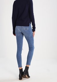 Tunna blåjeans med fransade fållar, gjorda av denim. Matchat med svarta ankelskängor med brun klack och en marinblå tröja.