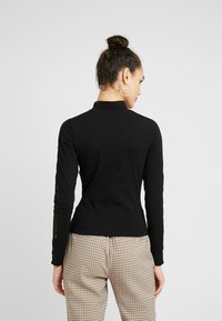 Black long-sleeve top with a high collar and lace detailing along the sleeves, paired with plaid pants. The fabric appears soft and fitted.