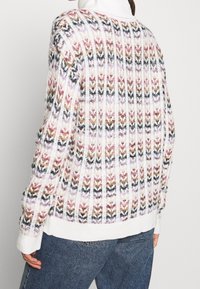 Strickpullover mit einem mehrfarbigen Zickzackmuster in Schattierungen von Pink, Braun und Schwarz. Gerippte Bündchen und Saum in Weiß.