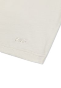 Gros plan sur un tissu beige avec le logo FILA cousu près de l'ourlet, montrant la texture et les détails de la couture propre.
