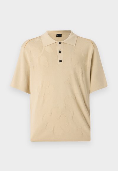 Beige pikétröja med en texturerad blommönster, treknapparsstängning och korta ärmar. Tillverkad av mjukt tyg med kontrasterande axelaccenter.