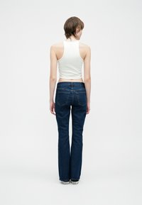 Canotta bianca aderente abbinata a jeans blu a zampa. I jeans presentano una vita media e tasche posteriori; tessuto liscio e aspetto classico in denim.